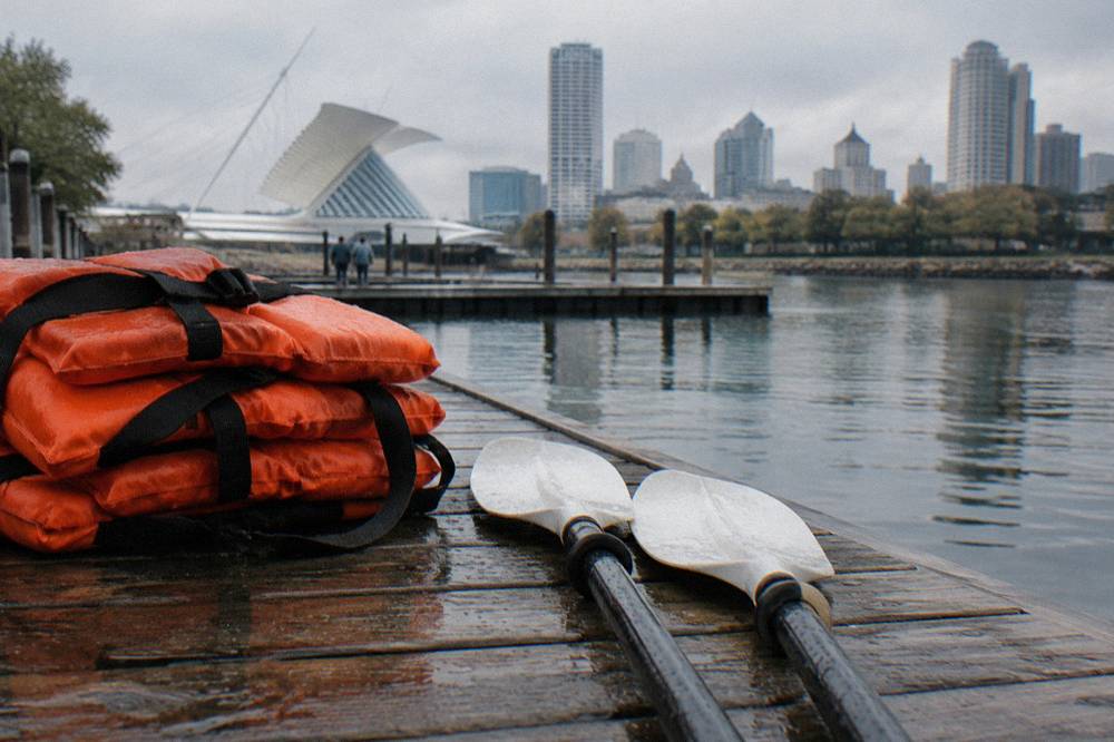 Life jackets and paddles laid out on a dock beside calm water