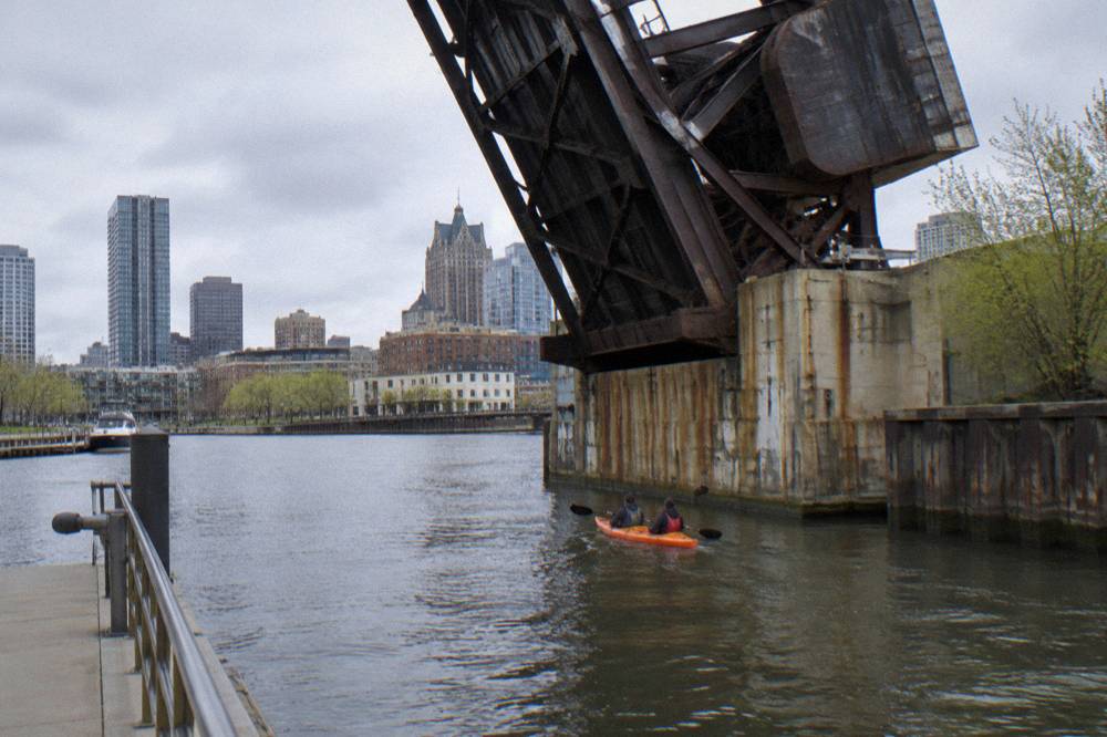 Tandem kayak passing under a downtown Milwaukee bascule bridge on the river