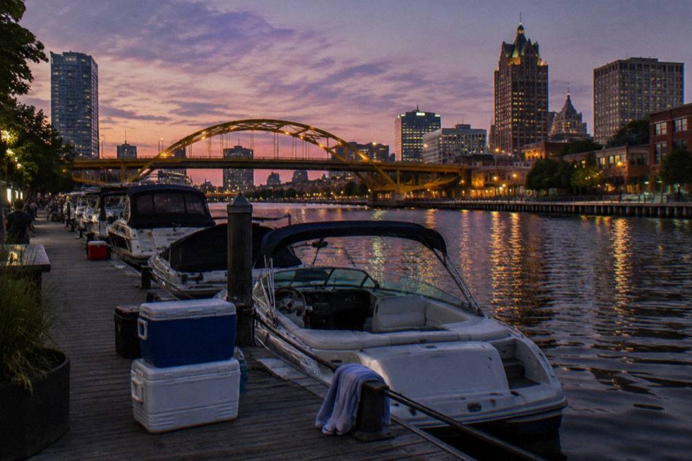 Crowded docks on the Milwaukee River at dusk with boats and lit bridges