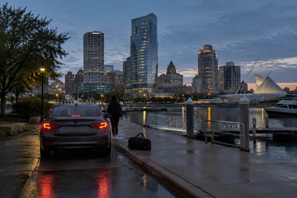 Rideshare car dropping passengers near a downtown Milwaukee river dock at dusk