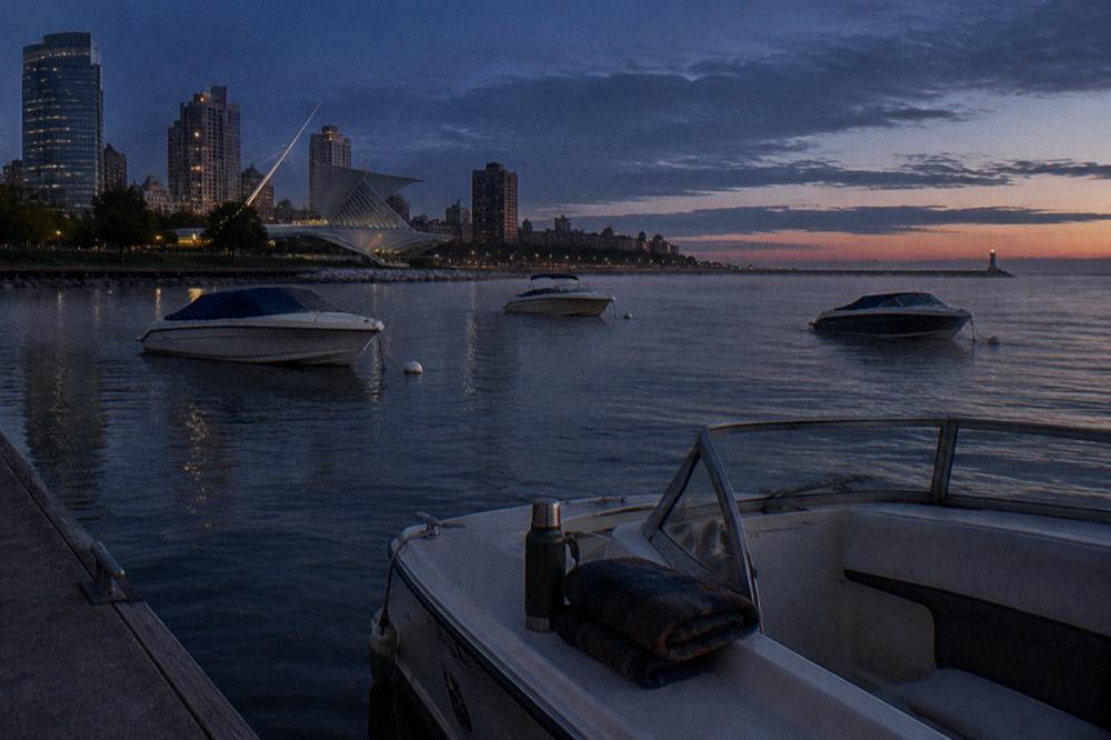 Small boats anchored on open water at dusk with a darkening sky over the shoreline
