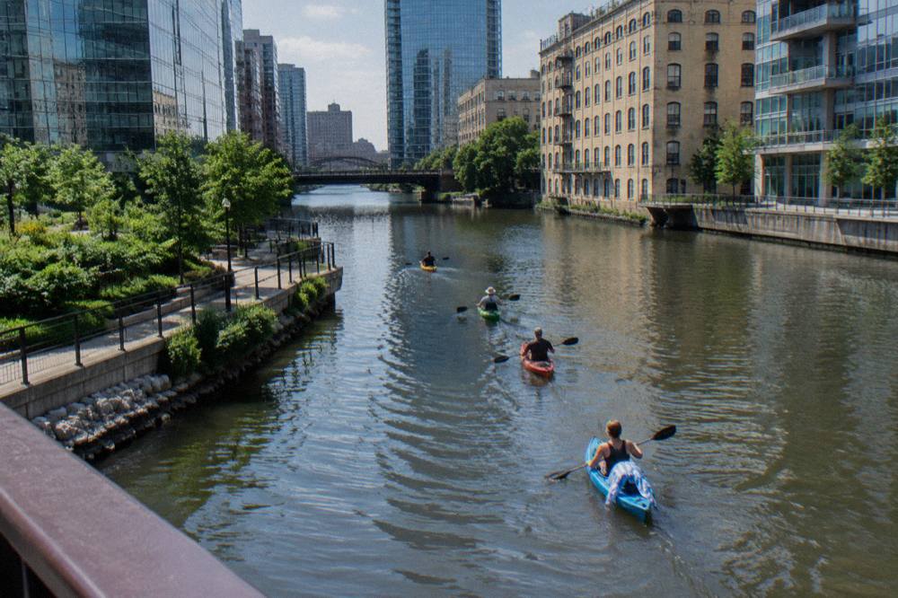 Kayaks floating on the Milwaukee River between downtown buildings on a sunny afternoon