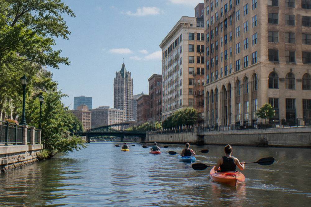 A small group of kayakers paddling together on the Milwaukee River with the downtown skyline above