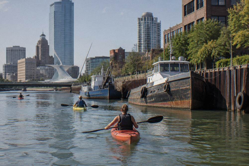 Kayaks paddling the calm Milwaukee River past downtown buildings