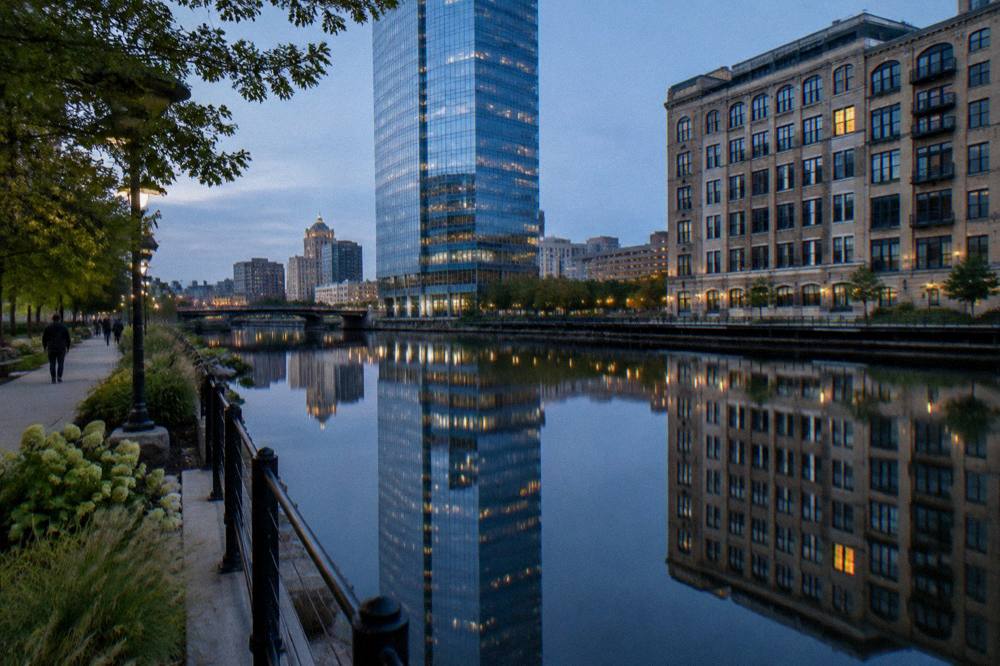 A wide river view of downtown Milwaukee buildings reflected in calm water