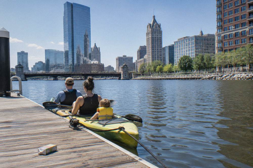 Kayaks tied at a dock on the Milwaukee River with the downtown skyline behind them
