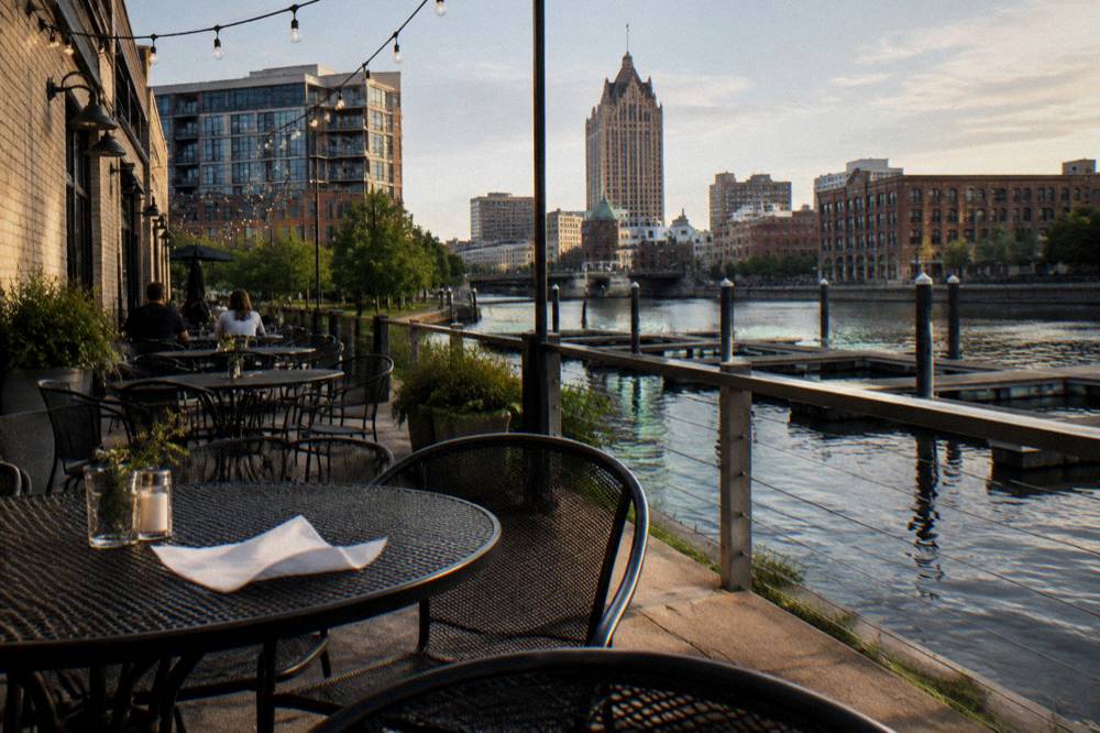 A stretch of the Milwaukee Riverwalk with tables and river docks in the afternoon light