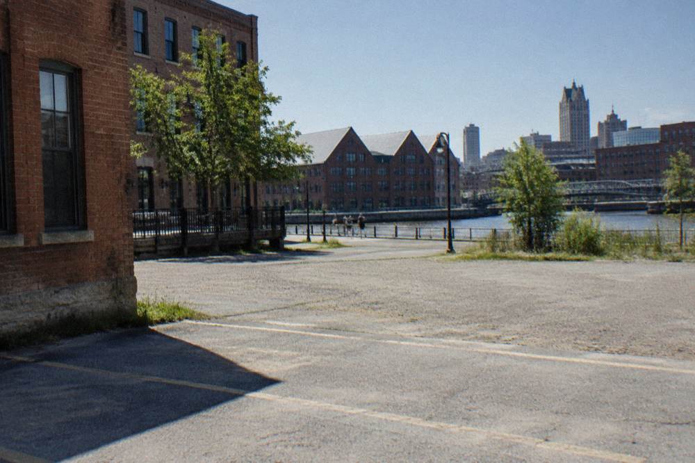 Paid surface parking lot beside brick buildings near a riverside street