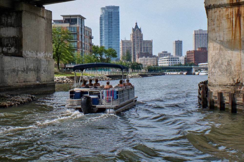 Pontoon boat carrying a small party moving along the Milwaukee River between bridge abutments