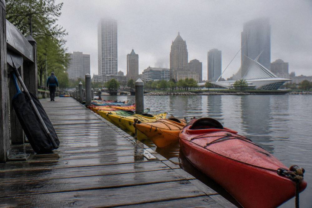 Kayaks resting on a dock on the Milwaukee River with the downtown skyline behind them