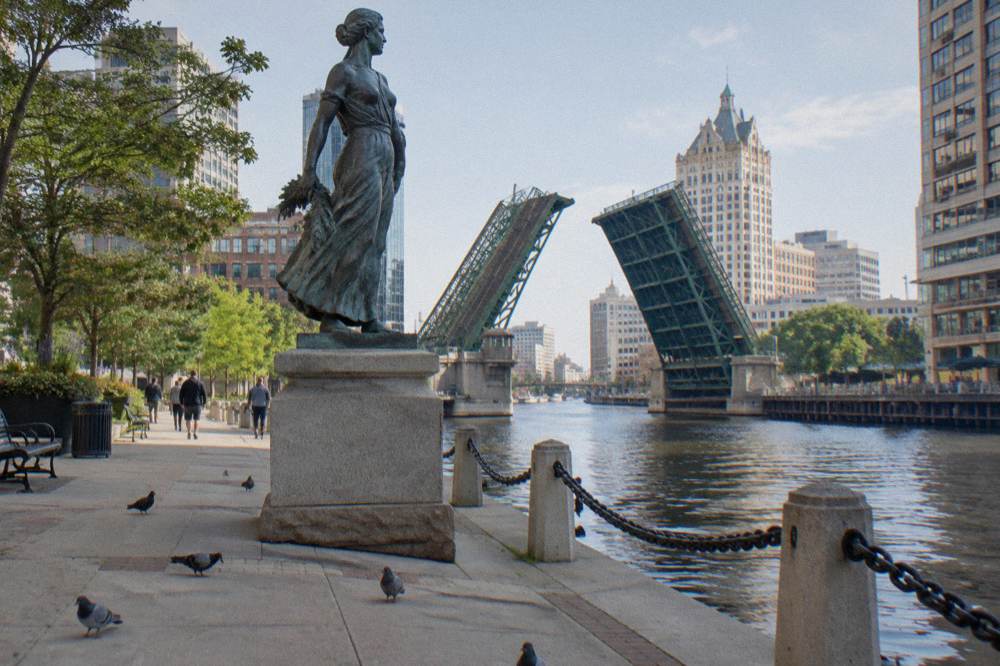 Bronze statue on the Milwaukee Riverwalk with the river and a bascule bridge behind it