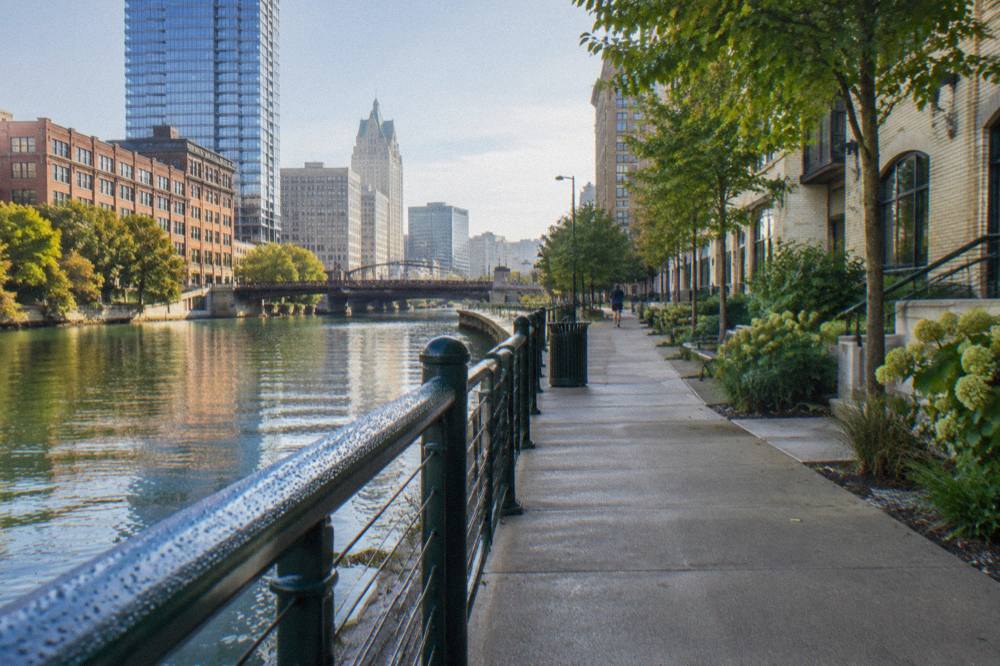 Concrete Riverwalk path beside the Milwaukee River with downtown buildings on both banks