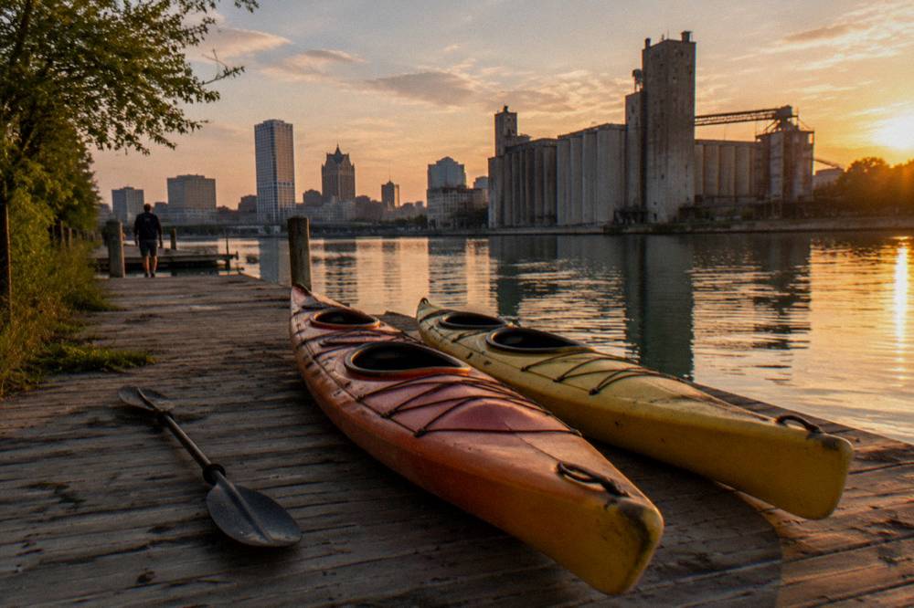 Empty kayaks pulled up on a dock on the Milwaukee River at golden hour